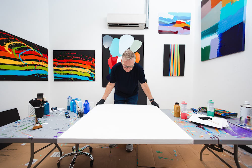 Photo of artist in studio standing before a blank canvas, face-up on a table with paint media, by Austin-based lifestyle photographer Nick Barnes.