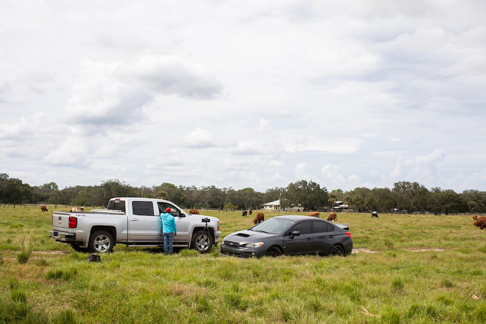 Behind the scenes photo of the photographer's and rancher's cars on ranch pasture after flooding from hurricane, cows in background.