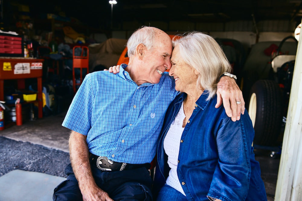 Photo of couple embracing, while smiling, with foreheads touching, seated in auto garage, by Altamonte Springs, Florida-based portrait photographer Brian Carlson.