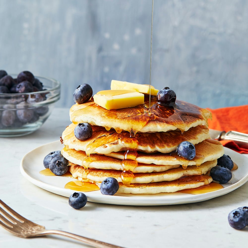 A stack of pancakes with blueberries, butter, and maple syrup drizzled all over. This is one of Trevor's images showcasing his expertise.