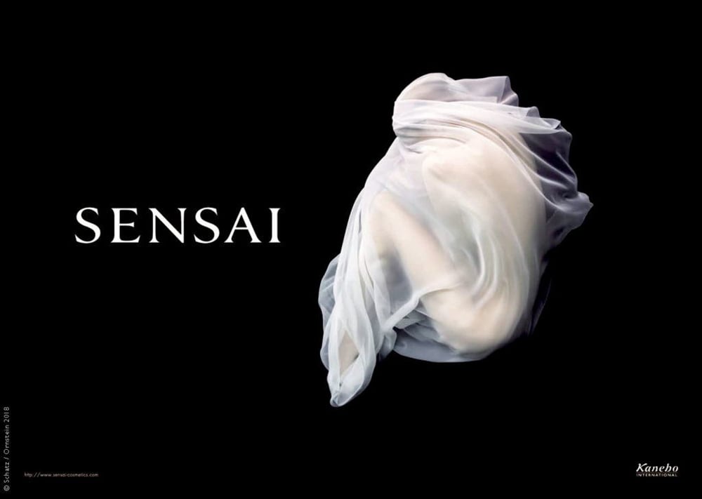 Underwater photo of a model covering in a translucent white cloth taken by Howard Schatz for Sensai. 