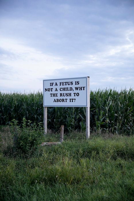 A sign in a cornfield reads "if a fetus is not a child, why the rush to abort it?"