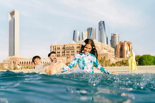 A family splashes in the water with the Abu Dhabi skyline in the background, shot by lifestyle photographer Tom Parker.