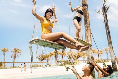 Friends swing over the ocean on the beach in Abu Dhabi, for their tourism campaign shot by Tom Parker.