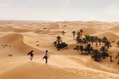 A man and woman carry sand boards up a dune in the desert in Abu Dhabi, shot by photographer Tom Parker.