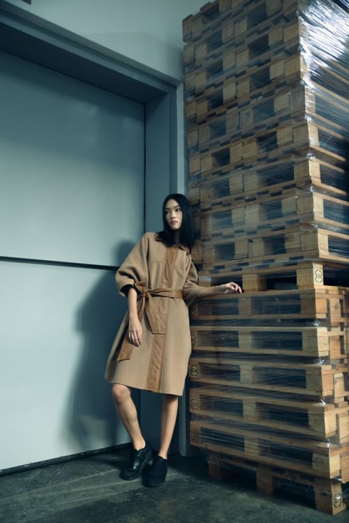 Photo by Boban James of a woman in a fashionable coat leaning on a stack of pallets in a loading dock.