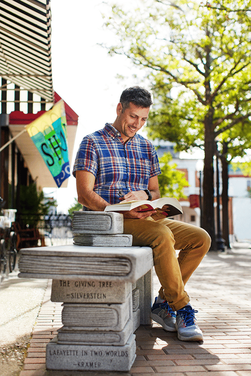 Man reading on a stone bench featuring famous book titles in Fayetteville, North Carolina.
