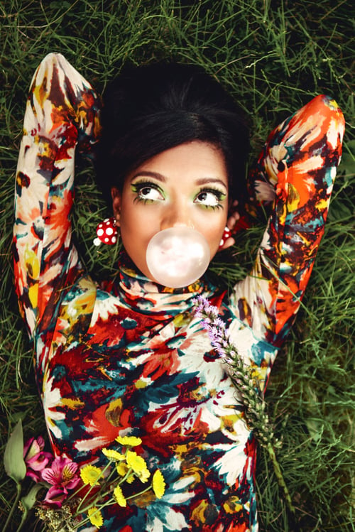 Photo by Kirsten Miccoli of a woman laying in the grass blowing a bubble with a colorful shirt.