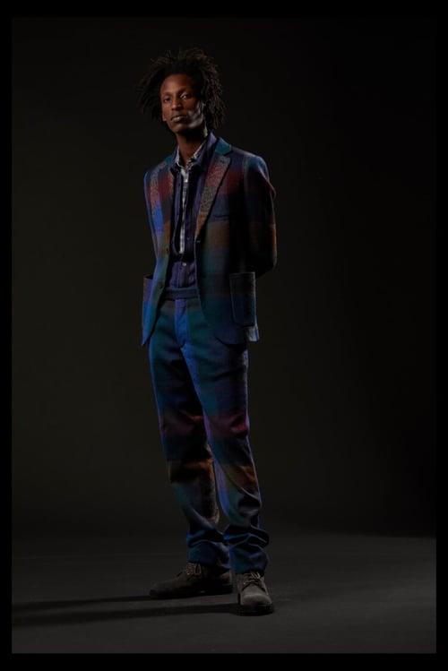 Photo by Luca Merli of a man standing in a dark studio room wearing a colorful, yet darkly-toned suit.