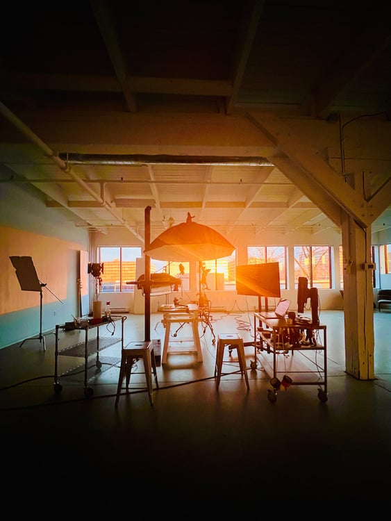 Behind-the-scenes photo of studio with food/drink set and photo equipment, with sun setting in background, by Montreal, Canada-based food/drink photographer David De Stefano.