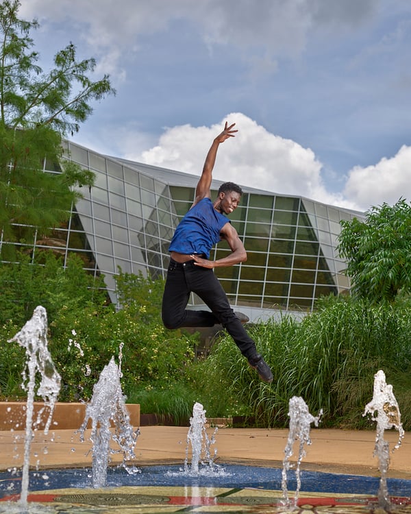 Portrait of ballet dancer leaping over fountain with one hand raised and one on side, by Tuscaloosa, Alabama-based music/performing arts photographer Michael J. Moore