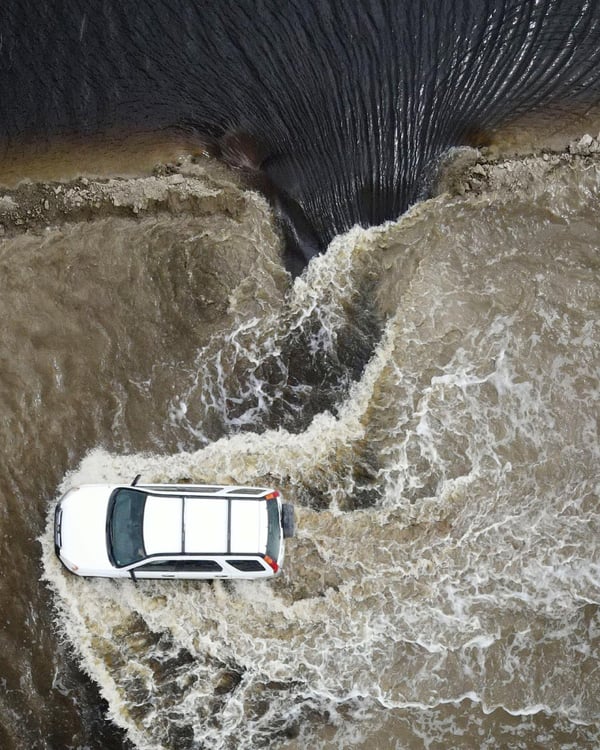 Photo by David Swanson of a car viewed from above driving through a flood.