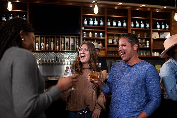 three friends laugh as they share drinks at a bar in Fayetteville, North Carolina.