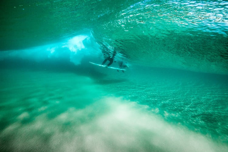 Photo by Adam Taylor of a surfer swimming under a wave.