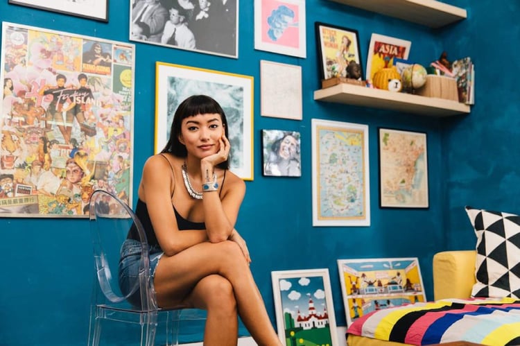 Photo by Juliana Tan of a woman in her studio posing with art she has collected.
