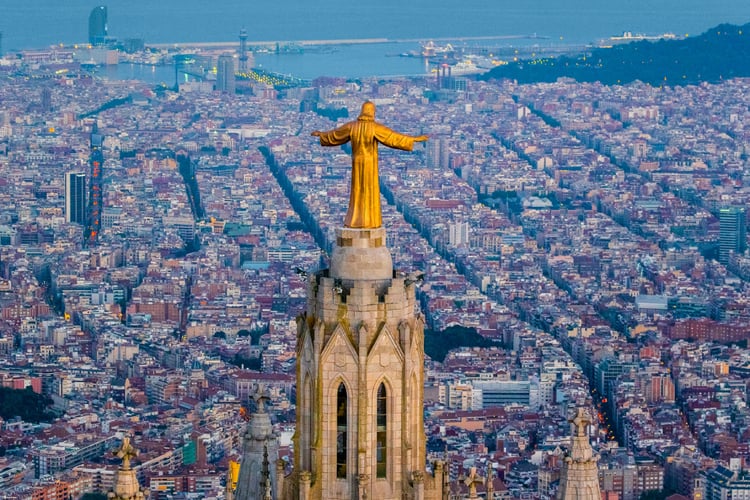 Photo by Vincent LaForet of a statue of Jesus on a cathedral's top looking over a city.