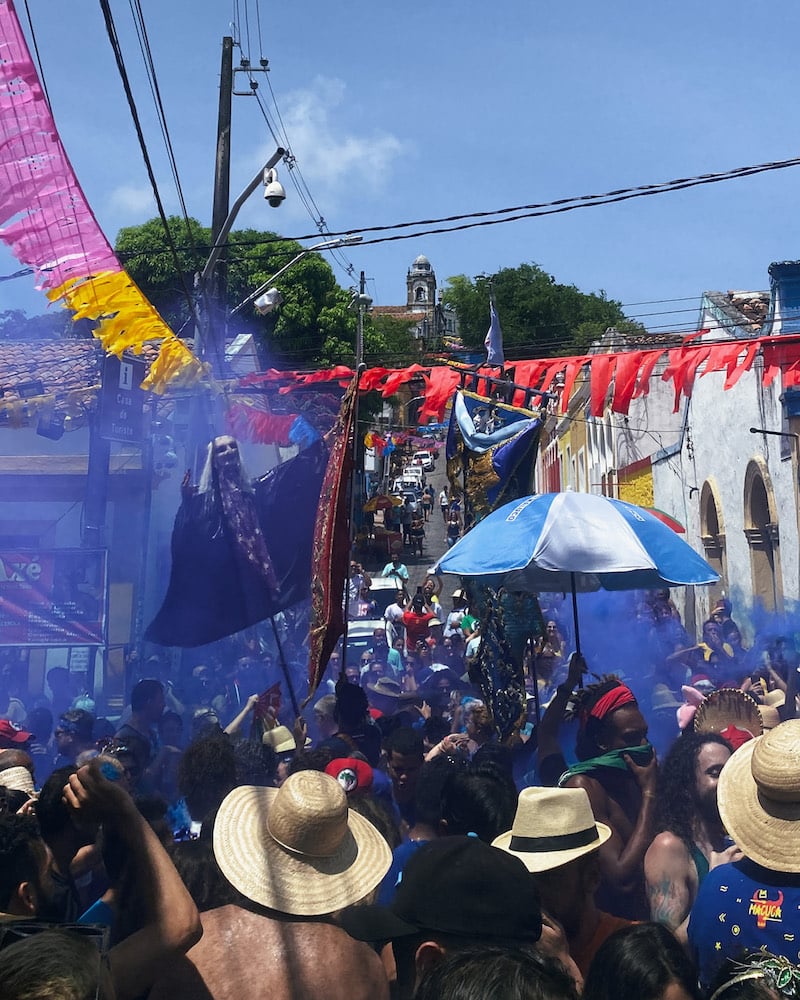 Street-view of revelers with streamers, banners, colorful smoke, and props at Carnival.