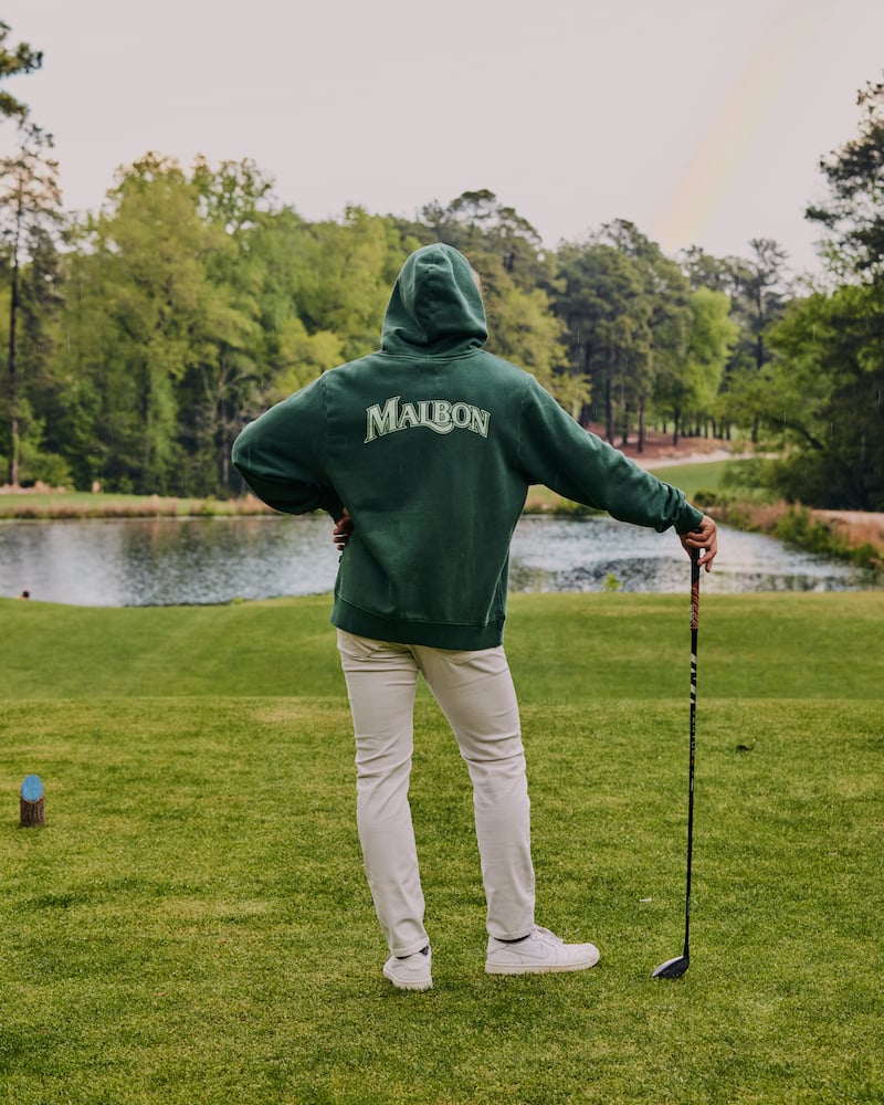 Image of figure in green hoodie standing back turned, holding a golf club, admiring a visible rainbow, by Charlotte, North Carolina-based fashion photographer Jackson Ray Petty.