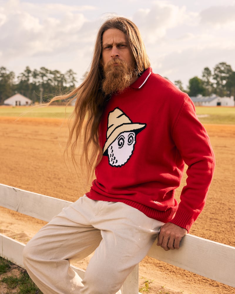 Image of long-haired bearded figure seated on horse fence in red sweater, making a solemn expression, by Charlotte, North Carolina-based fashion photographer Jackson Ray Petty.