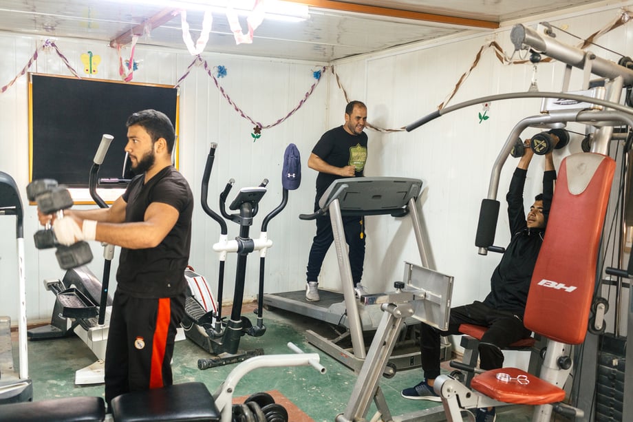 Bradley Secker's shot of men lifting weights and using a treadmill in a small room with gym equipment