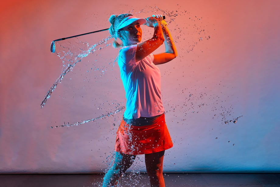 Female golfer follows through with a swing as she is doused with strategic shots of water.