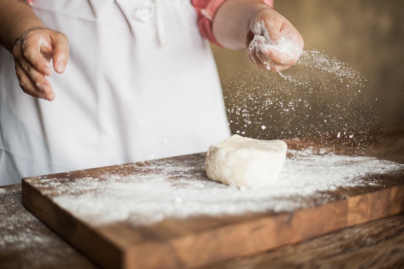 Close-up image of Nicole Mournian sprinkling flour onto her work surface and a block of pastry that is ready to become a delicious pie.