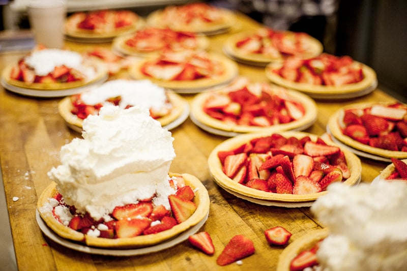 Image of many strawberry pies in the making on a rustic wooden worktop captured by Alan Gastelum.