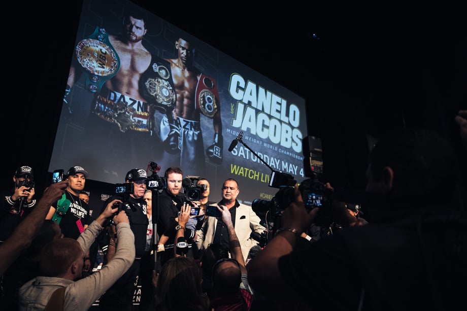 AK Collective snaps a press conference as it happens in front of a Canelo vs. Jacobs billboard