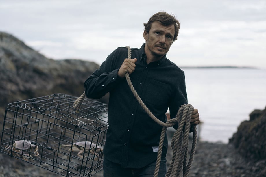 Simon Whitfield carries a crab trap over his shoulder by a rope while wearing an Anian wool Oxford shirt