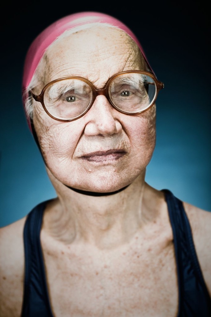Photograph of a bespectacled lady with wisps of silvery-white hair poking out of her pink swim cap.