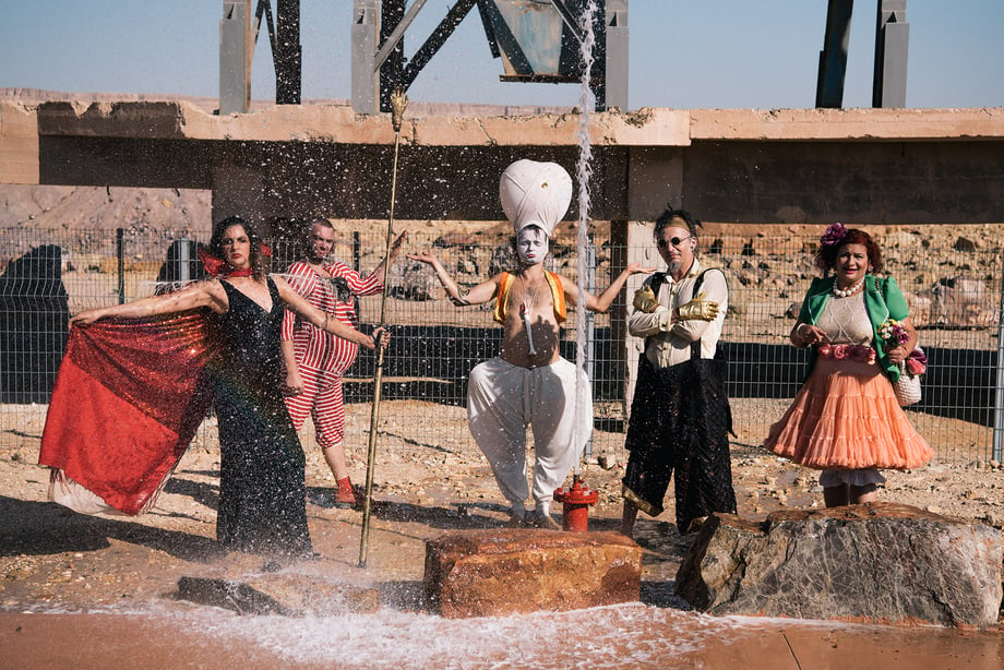 Arik Shraga and DAVAI Theater group in the dry sand as water spurts up from a fire hydrant