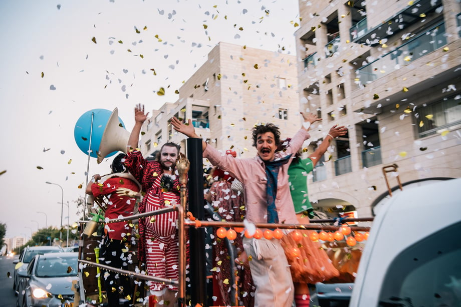 Arik Shraga photographs the DAVAI Theater group as they move down the street in their trailer as confetti falls from the sky