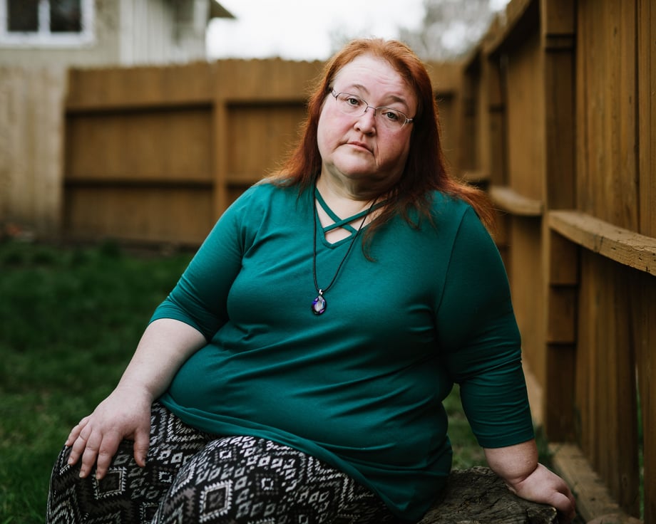 Picture of a woman sitting in a yard next to the fence.