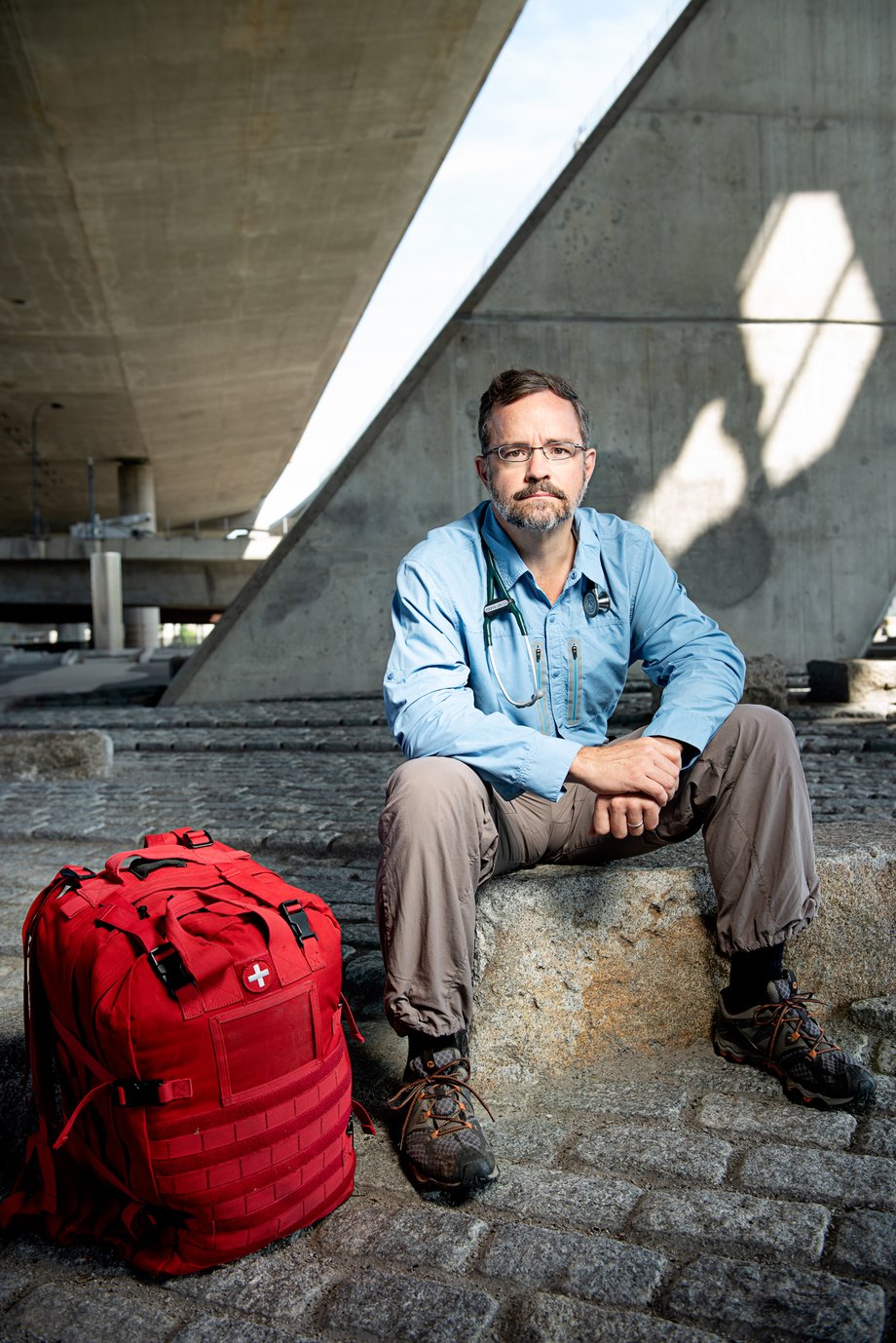 Webb Chappell's portrait of Dr. Harris, sitting on a rock beneath an underpass with a large, red medical bag