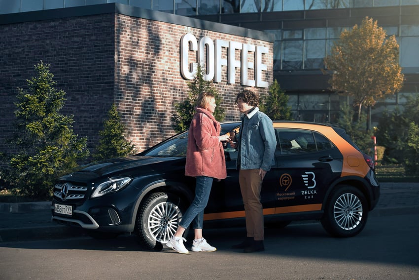 Stanislav Solntsev photographs a young couple standing by a Belka car next to a coffee shop
