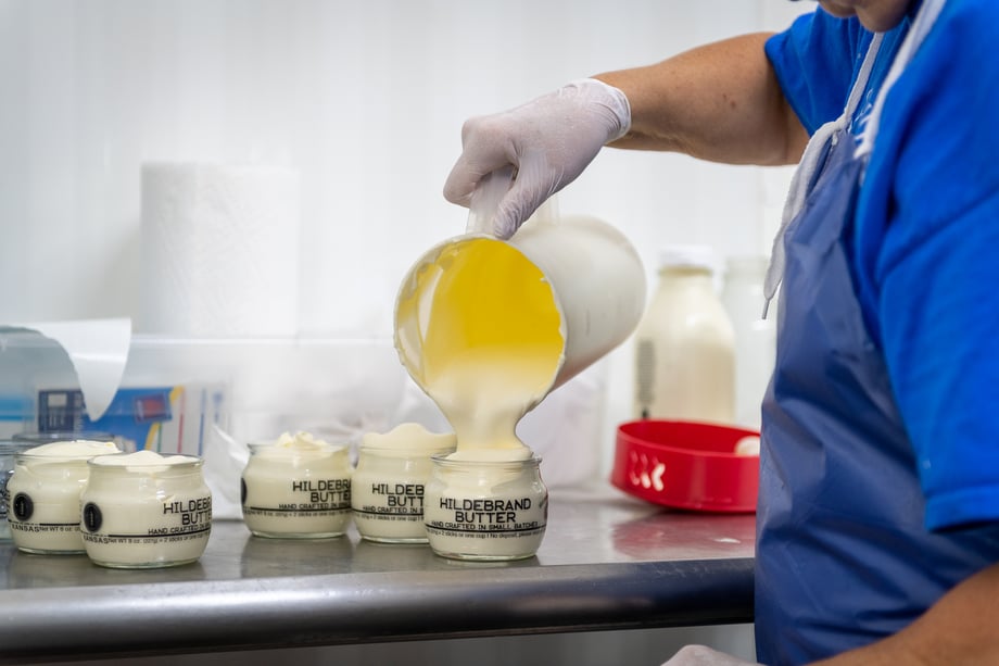 Chad Holder's closeup of a dairy worker pouring fresh butter into small glass jars labeled Hildebrand Butter