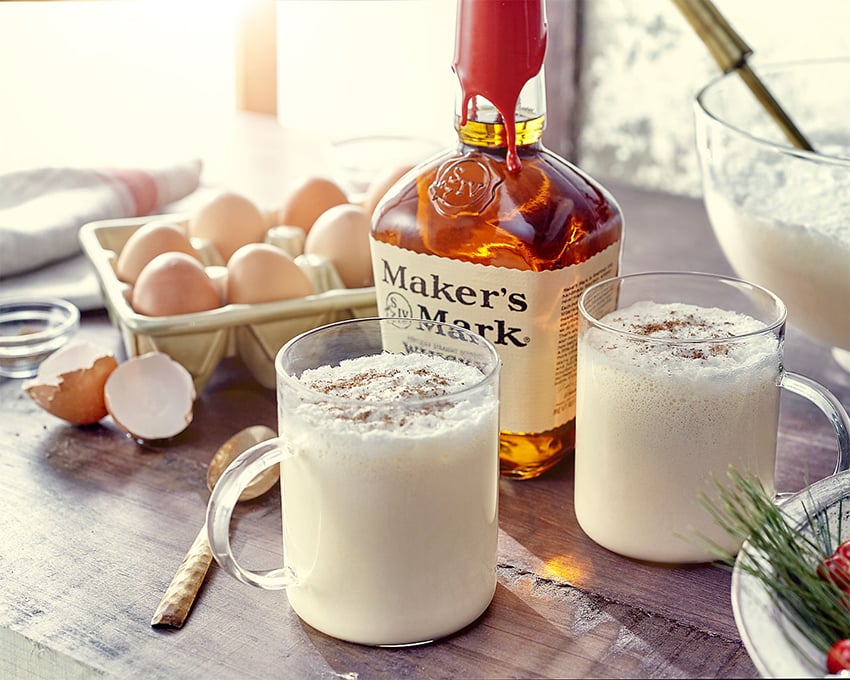 Two egg nogs heaping with nutmeg before a bottle of Maker's Mark in this photo by Terri Campbell