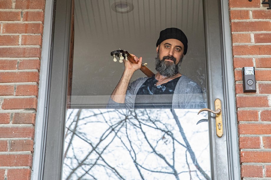 Photo of a musician looking out of the window of his door holding a banjo.