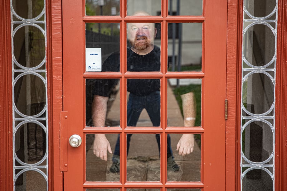 Shot of a man through a glass paneled door with the photographer's reflection showing an optical illusion of the man having unusually small legs.