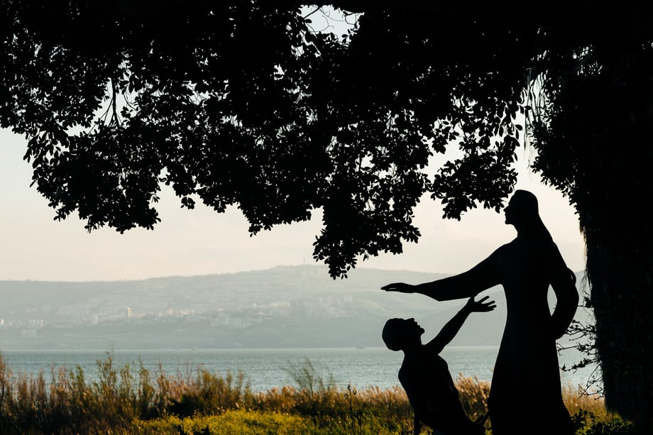 A Statue of Jesus and Peter is shown in silhouette under a tree against the river in the background