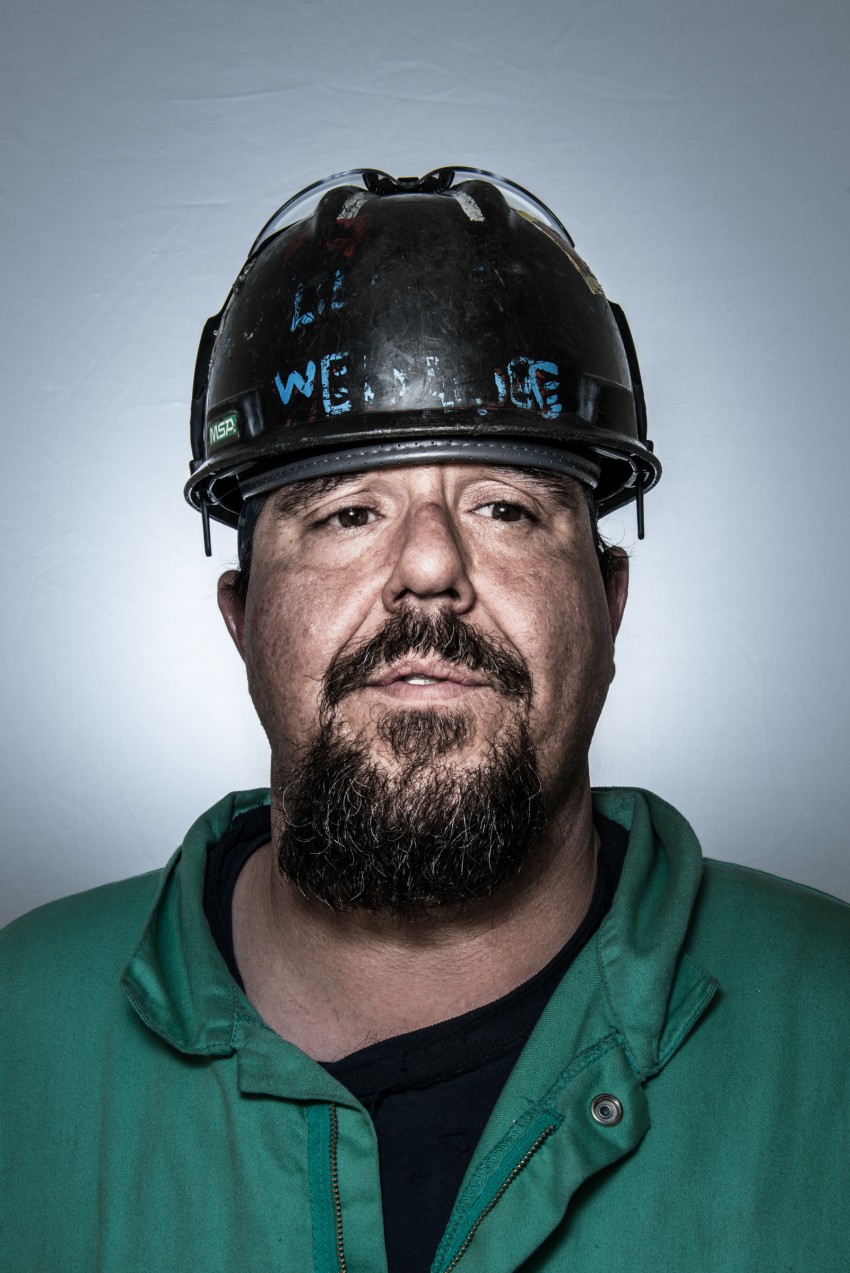 Heather Perry's portrait of ship builder Tim, wearing a green polo shirt and hard hat