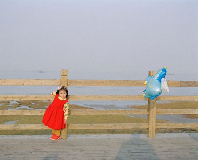 A little girl holds a unicorn balloon as she poses along side the Huangpu river, photo by Jonathan Browning.