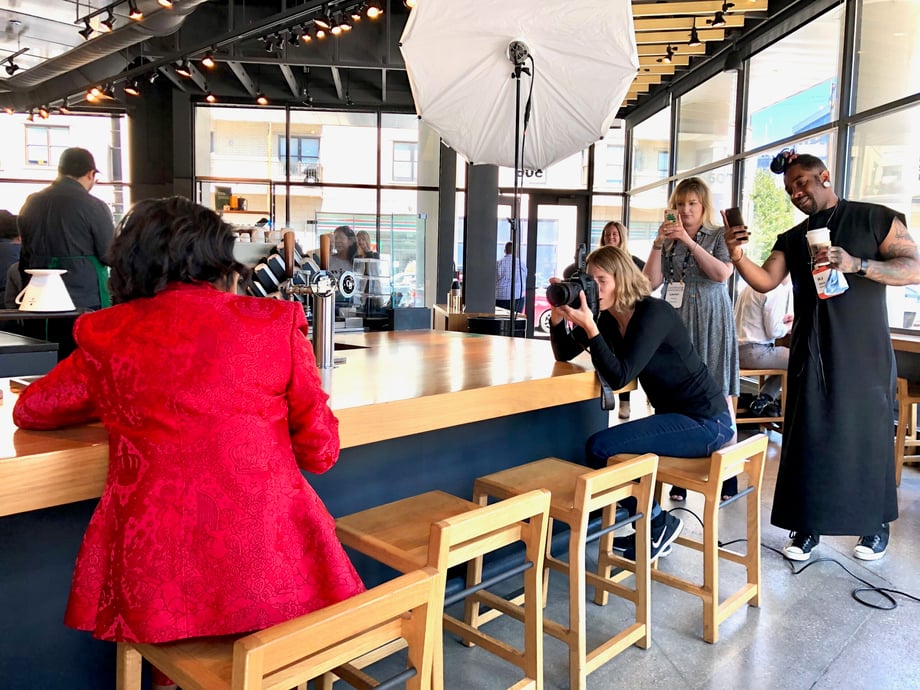 Crew members stand behind Sara Stathas as she photographs Roz while sitting at the counter at Starbucks