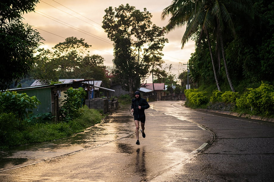Ian MacLellans photo of man wearing Janji running on the road in the rain, with the sun bouncing off the slick pavement