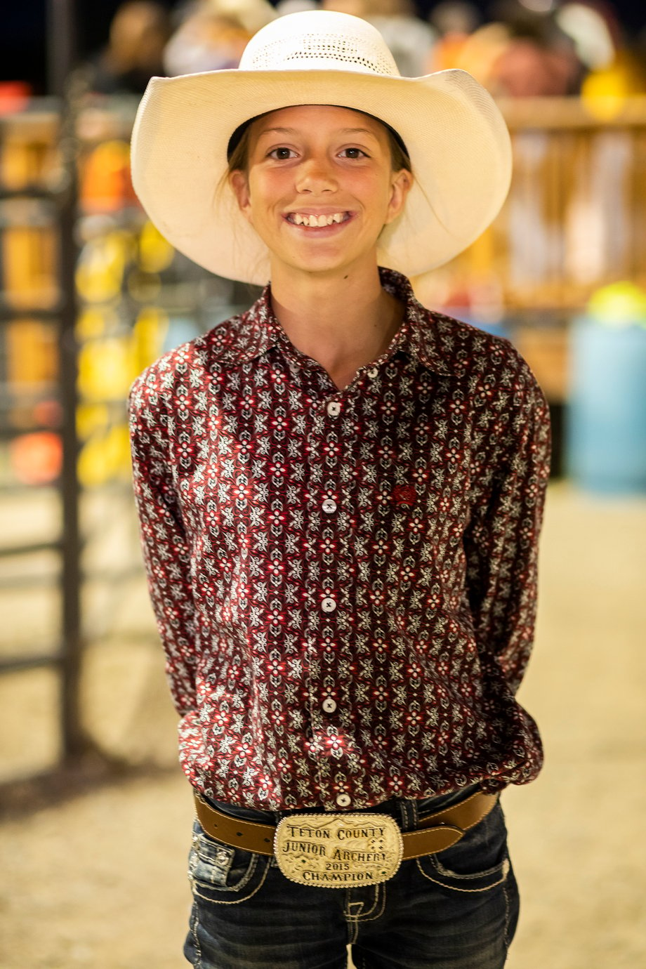 A child in a cowboy hat poses for Adam Hester; his belt buckle says Teton County Junior Archery Champion 2015