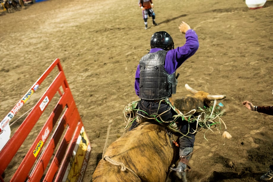Adam Hester catches the feeling of riding a bull as a rider is let loose out of the gate wearing a safety vest and helmet