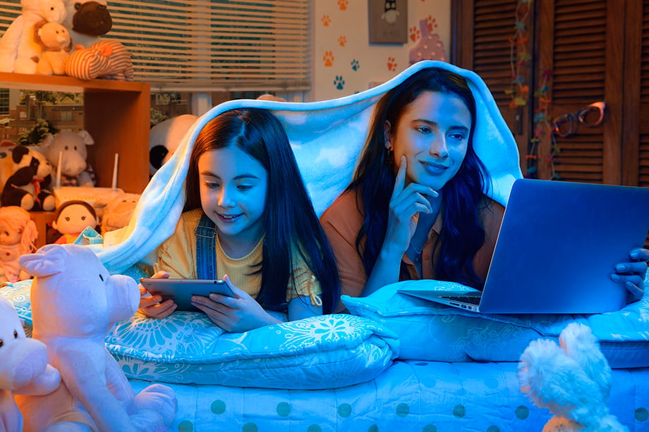 A younger girl and her sibling share a blanket while watching shows on a computer screen and tablet. Image shot by Jorge Oviedo for ETB. 