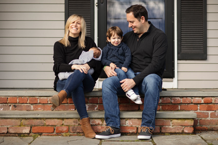 Josh Behan's COVID project Front Porchtrait shows smiling parents on brick steps with a toddler and newborn baby