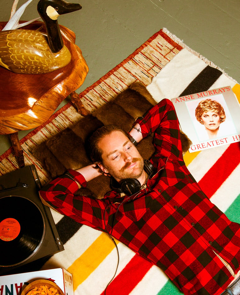 Man lying on the floor in a red and black plaid flannel shirt, listening to an Anne Murray's record shot by Vancouver-based portrait photographer Kamil Bialous