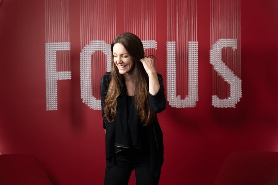 Photo by Kevin Heagney of Kat Cole in front of a blurred sign that says FOCUS